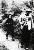 A diminutive female Vietnamese militia woman drives a captured Chinese PLA soldier ahead of her during the 1979 Chinese invasion of Vietnam (the Third Indochina War). The image is strikingly (and perhaps deliberately) reminiscent of a similar photograph from the Second Indochina War showing a large American pilot being driven by a tiny Vietnamese female soldier.